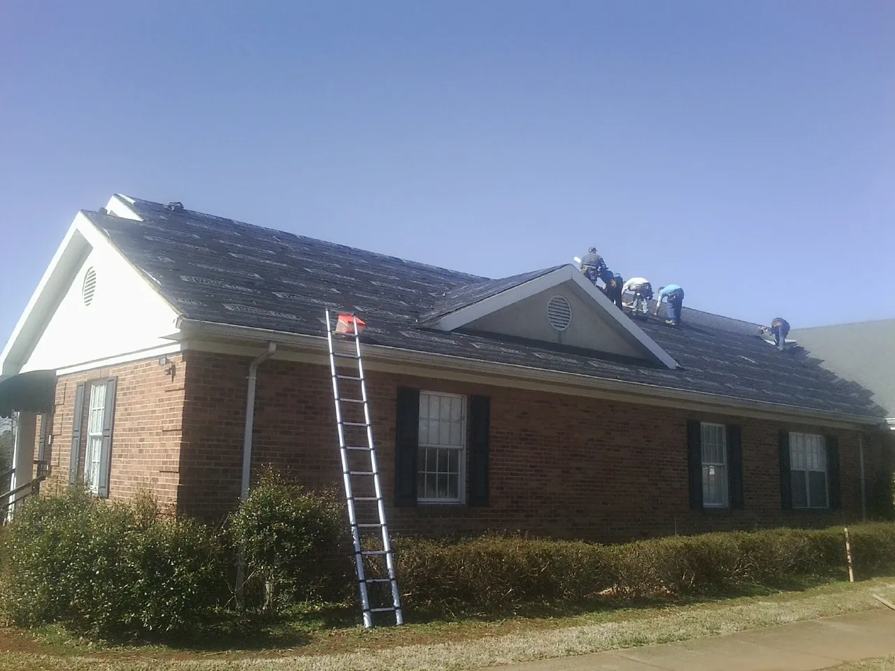 Crew tearing shingles off a brick ranch roof with a ladder set — Metal Roof Repair work by our crew in Little Hocking