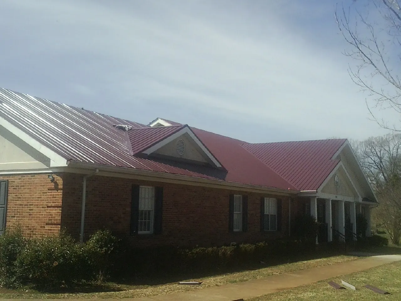 Red metal roof with gabled entries on a long brick building, from a Hail Damage Roof Repair job in Little Hocking