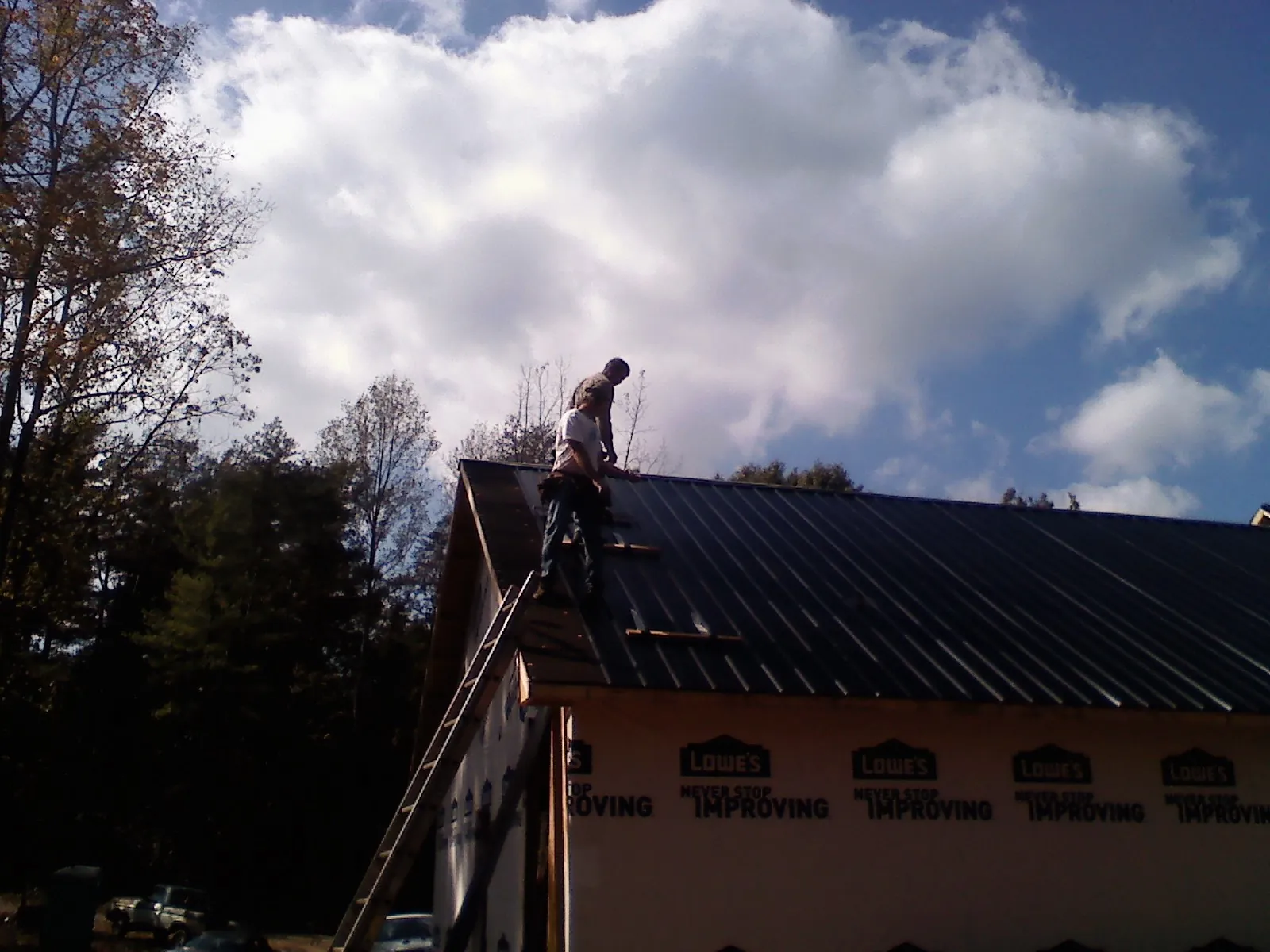Roofer fastening dark metal panels high against a cloudy sky, from a Roof Inspection job in Little Hocking