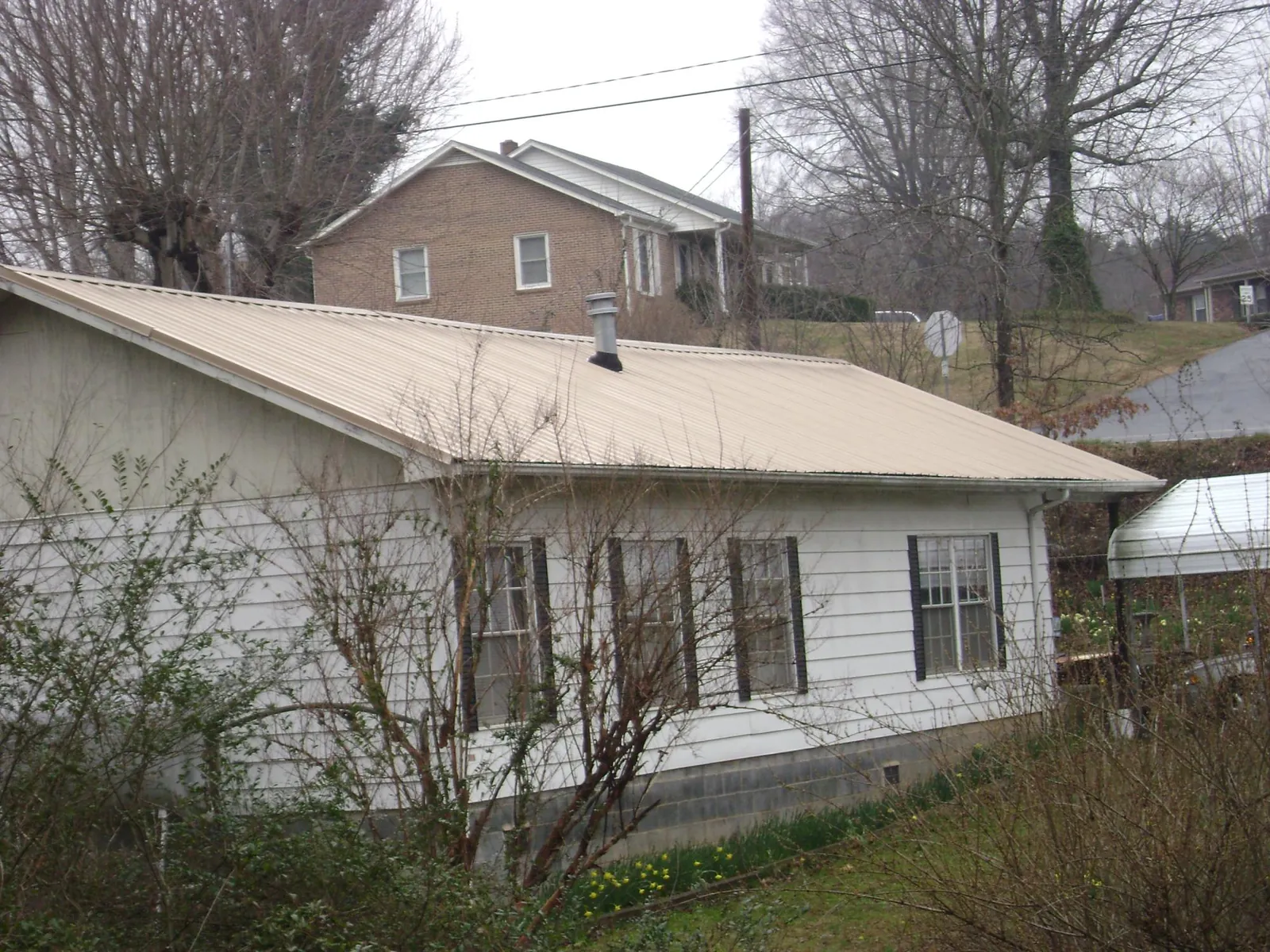 Tan metal roof on a white sided house set into a hillside — Commercial Roofing by Roofing Brothers in Little Hocking